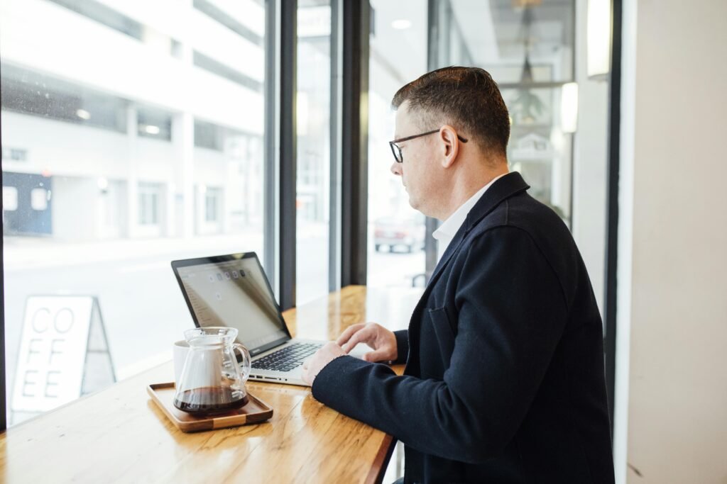 Businessman in a cafe working on a laptop with coffee by the window. Modern and professional setting.